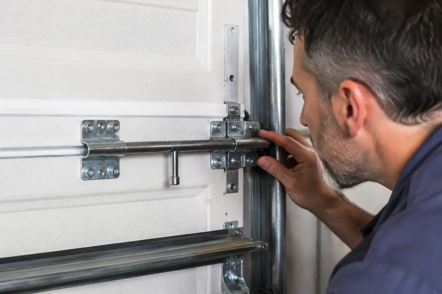 Person leaning close to a white paneled door, one hand on a metal slide-bolt bar mounted across the panel. — Garage Door Manual Lock Repair, Burlington